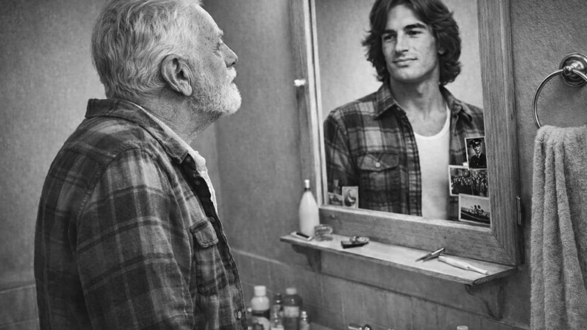 An older man looks in a mirror and sees his younger self reflected back